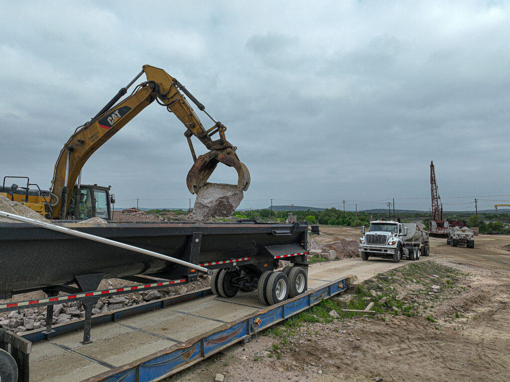 A crane loading granite armor stone on to a large truck